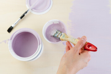 Hand with brush and cans of mauve paint. Copy space. Top view.