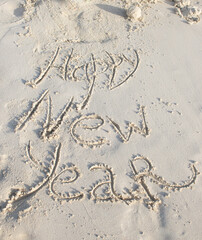 Inscription Happy New Year written in white sand of a beach. Celebrating the New Year in hot countries. New Year and travel content.