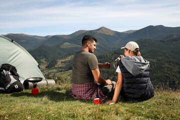 Couple with coffee enjoying mountain landscape near camping tent, back view