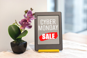 Cyber Monday sign on e-reader electronic book next to artificial pink orchid on the kitchen table with a linen tablecloth by the window