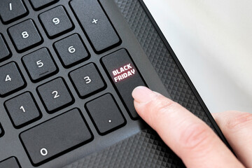 Keyboard corner of black laptop with female finger clicking on Black Friday button. Shopping concept