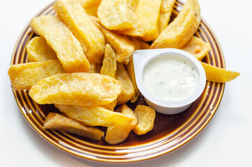 Deep fried and crispy delicious fries on the ceramic plate with garlic dip
