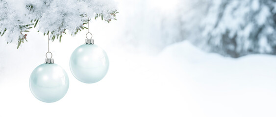 Gläserne Weihnachtskugeln an einem Tannenzweig vor einem verschneiten unscharfen Hintergrund