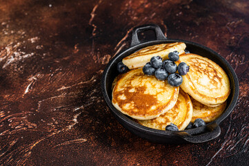 Fried Pancakes with fresh blueberries and maple syrup in a pan. Dark background. Top View. Copy space
