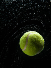 Yellow tennis ball with water splashes on a black background
