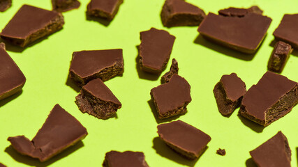 Closeup of broken, crushed dark chocolate bars stack isolated over green background