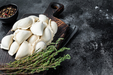 Frozen raw dumplings pierogi with potato on a wooden board. Black background. Top View. Copy space