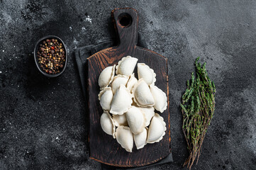Frozen raw dumplings pierogi with potato on a wooden board. Black background. Top View