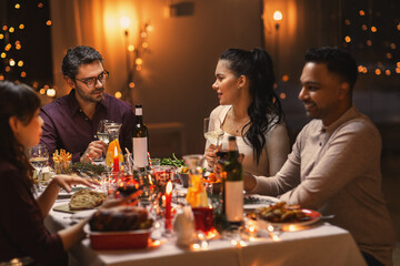 holidays, party and celebration concept - multiethnic group of happy friends having christmas dinner at home and drinking wine