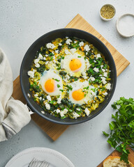 Traditional mediterranean green shakshouka fried with eggs, spinach, celery, salty sheep milk cheese, seasoning and pepper. Served in pan on wooden cutting board. Overhead, vertical