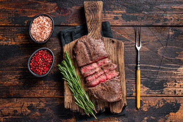 Fried Top Blade or flat iron roast beef meat steaks on wooden board with rosemary. Dark wooden...