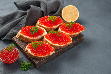Sandwiches with red caviar, butter and lemon on a dark background. Side view, copy space.