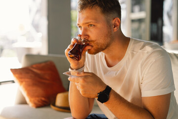 A man with mustache drinks and enjoy Turkish traditional hot tea in the lobby of a Turkish hotel. Turkish tea and traditional turkish culture concept.