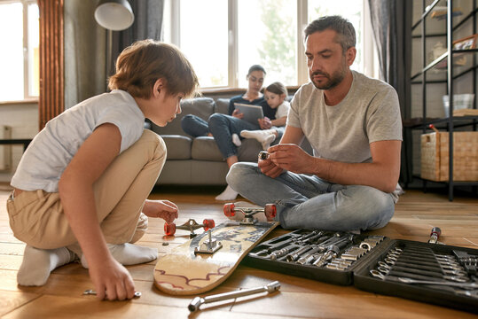Caucasian father teach teenage son repair skateboard