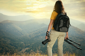 Professional photographer with modern camera and tripod in mountains, back view. Space for text