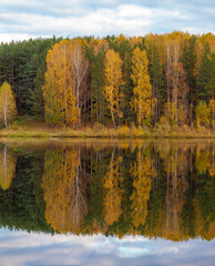 Colorful foliage tree reflections in calm pond water on a beautiful autumn day. A quiet and beautiful place to relax.