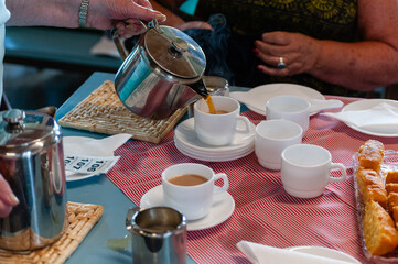 Cups of tea and raffle tickets. One person seated while another person pours from a teapot.