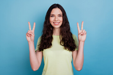 Photo of cheerful positive girl show v-sign shiny white smile posing on blue background