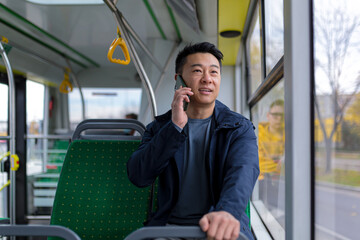 asian man in public bus passenger having fun talking on mobile phone, in casual clothes