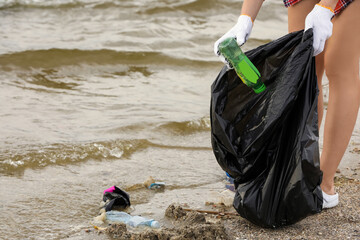 Woman in gloves with trash bag collecting garbage on beach, closeup