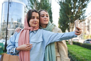 Optimistic muslim girls in headscarfs is making selfie while walking together