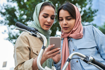 Girls of islamic religion using app near city bicycle station, social network