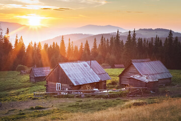 small wooden house in the mountains. incredible sunset over the top of the mountains. rays of the sun.