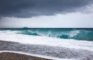 Mediterranean sea with stormy weather and big waves. Wave breaking on the beach. Turquoise water and ship on the horizon. Sicily, Italy.