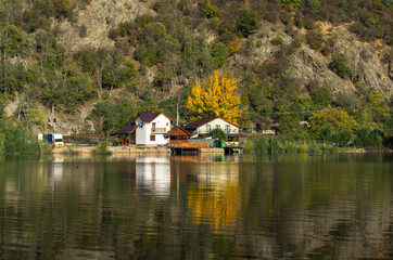 Fototapeta na wymiar The house is located in a beautiful landscape, on the edge of the lake. The autumn. Reflections in the water.