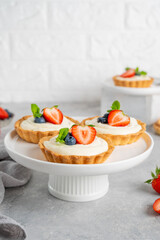 Delicious mini tarts with fresh berries and custard on a white plate on a gray concrete background. Copy space