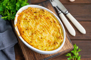 Homemade Shepherd's Pie in the casserole dish on a dark wooden background. Traditional British dish with minced meat and mashed potatoes.