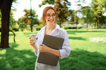 Happy girl student in glasses and white shirt holds laptop and cup of coffee, banner. Education