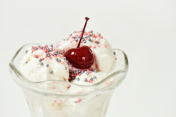 Close up of white vanilla sundae ice cream in cup with sweet grains and bing cherry on top isolated on white background