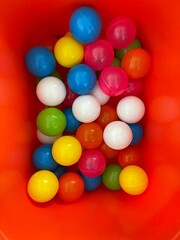 Fototapeta na wymiar Top view shot of many colorful plastic balls in red container in childrens room