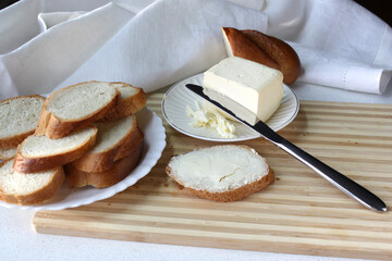 Pieces of white bread are buttered on a wooden cutting board. Breakfast on the background of a white linen napkin.