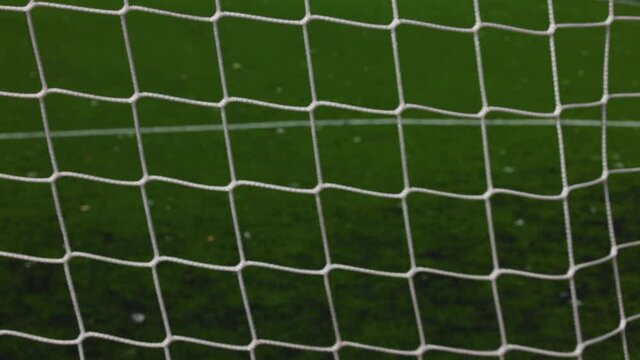 Football ball scoring in goal net over green pitch