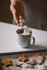Woman puts marshmallows in a hot cocoa mug. Festive atmosphere
