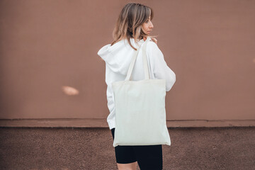 White cotton bag on woman's shoulder. Mock up, zero waste concept.