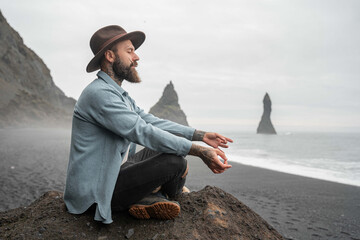 Mindful bearded man sitting at the rock and practicing yoga while enjoying meditation