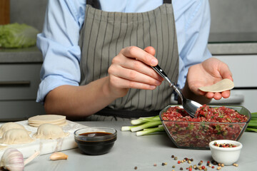 Woman making gyoza at light grey table, closeup