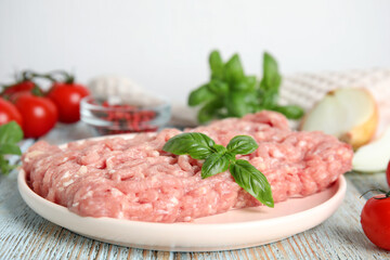 Raw chicken minced meat with basil on light blue wooden table, closeup