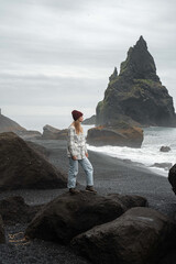 Woman standing at the black beach in Iceland with stormy ocean waves and cloudscape