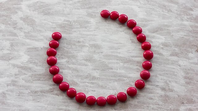 Stop motion video with a smiling positive emoticon appearing. Animation of a smiley made of red sweets on a light background painted with a brush.