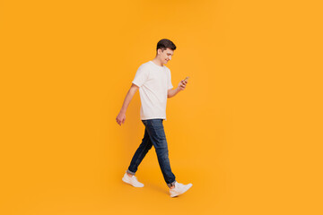 Fototapeta na wymiar Profile portrait of energetic friendly guy hold cellphone look screen step go on yellow background