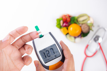 Woman test blood glucose for diabetes with glucometer over fresh food background. World diabetes day awareness concept, 14 November.