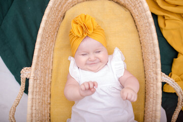Cute baby posing in a wicker basket and smiling. A fashionable baby in a yellow hat