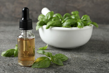 Glass bottle of basil essential oil and leaves on grey stone table, space for text