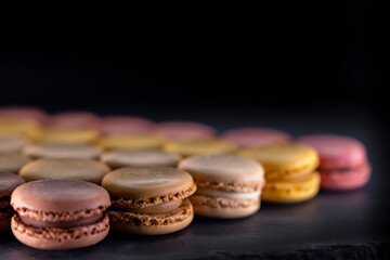 chocolate, coffee, vanilla, lemon and strawberry macaroons on black background
