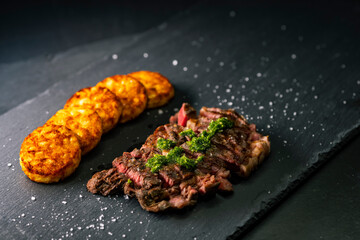 beef steak with potato patties on a dark background