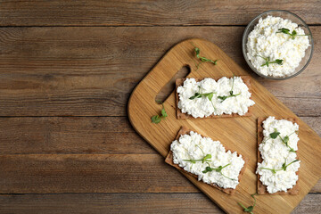 Fototapeta na wymiar Crispy crackers with cottage cheese and microgreens on wooden table, flat lay. Space for text